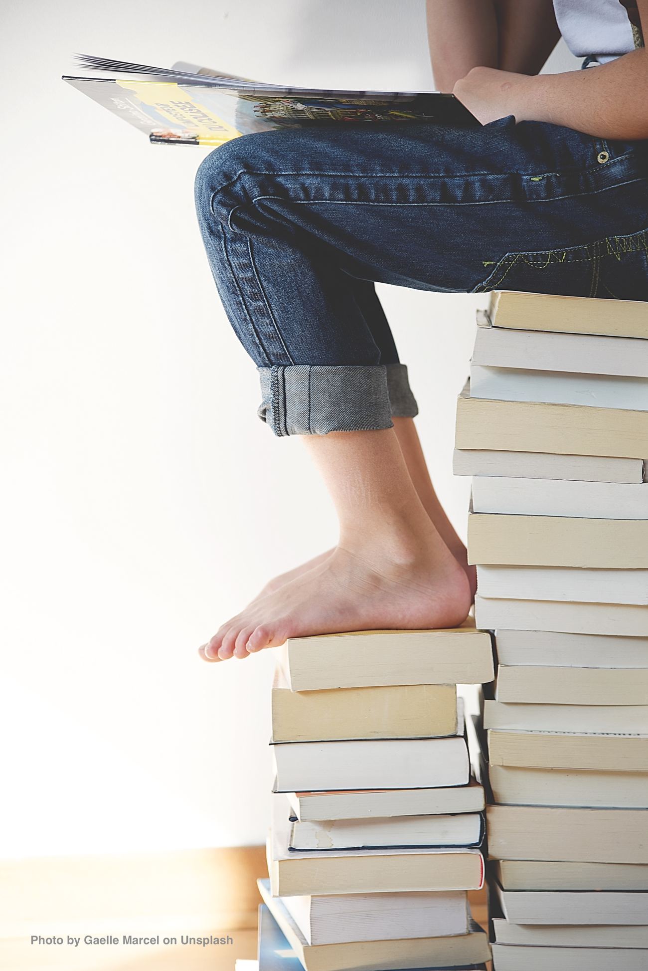 Beine in Jeans und nackte Füße auf Bücherstapel